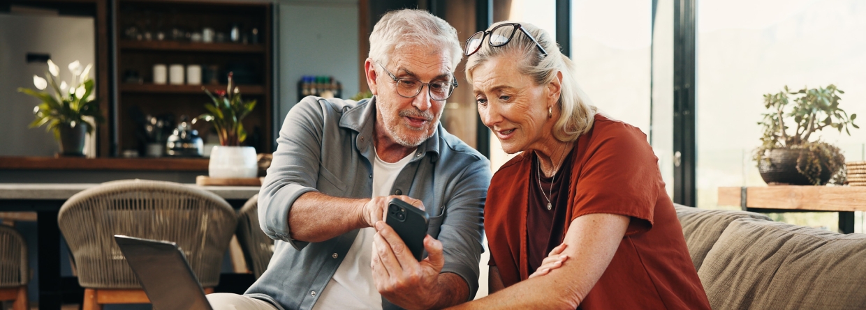 Een ouder stel kijkt op een telefoon en laptop
